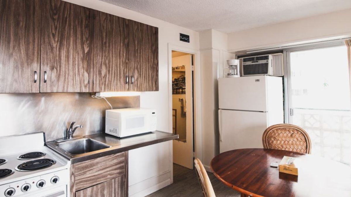 A kitchen with wooden cabinets, a stove, sink, microwave, refrigerator, round table with chairs, and a window with curtains.