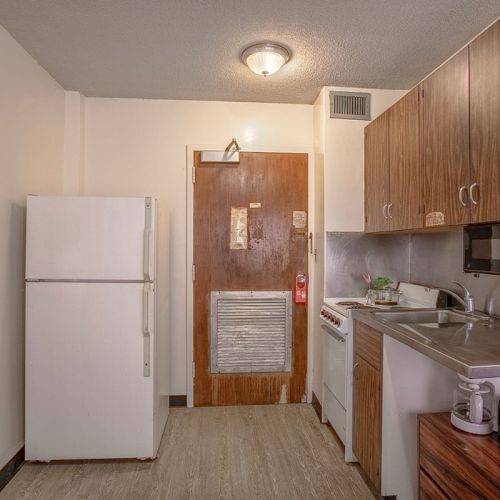 This image shows a small kitchen with a refrigerator, microwave, sink, stove, and cabinets, and a door leading out of the room always ending the sentence.