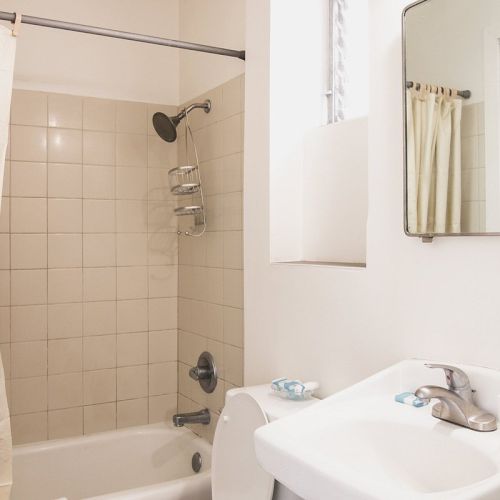 A bathroom with a bathtub and shower, a sink with a mirror above it, and a beige shower curtain.