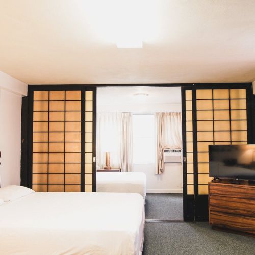 A bedroom with two beds, a TV on a wooden stand, and sliding shoji doors revealing another bed in an adjoining room.