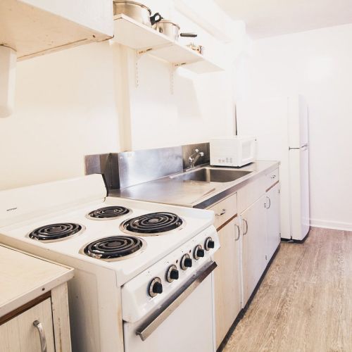 This image shows a small, well-lit kitchen with a stove, countertops, sink, white refrigerator, and wooden cabinets.