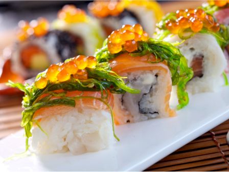 The image shows a plate of sushi rolls topped with seaweed and fish roe, arranged on a bamboo mat.