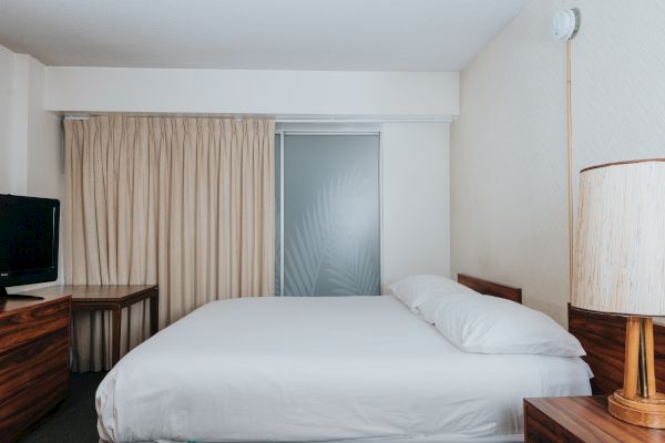 The image shows a minimalist hotel room with a bed, TV, desk, and lamp, neutral tones, and a frosted glass door with a leaf design ending the sentence.