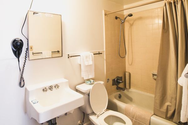 A bathroom with a sink, mirror cabinet, toilet, bathtub with shower, towels, and a wall-mounted hairdryer.