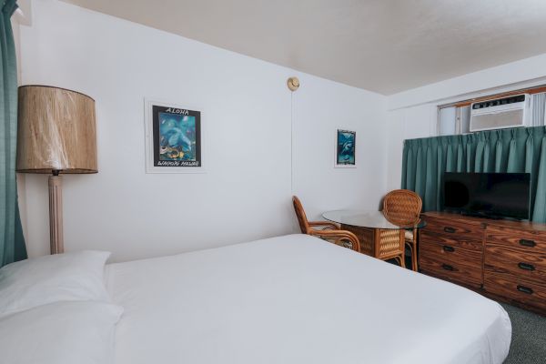 A hotel room with a bed, wicker furniture, framed pictures, a TV on a dresser, and an air conditioner, all in a cozy setting, ending the sentence.