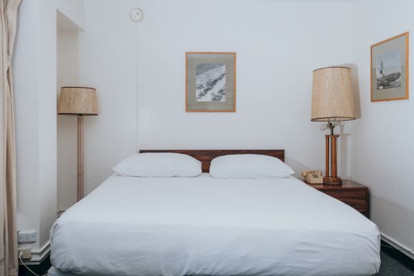 A neat bedroom with a large bed, two lamps on either side, and framed pictures on white walls.