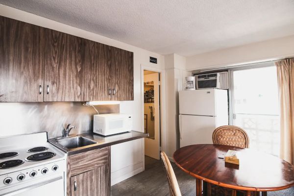 A small kitchen with a stove, sink, microwave, refrigerator, and a round dining table with chairs near a sliding door.