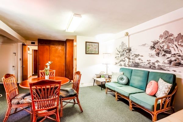 A cozy living room with a green sofa, a round wooden dining table with wicker chairs, and a large wall art piece, ends the sentence.