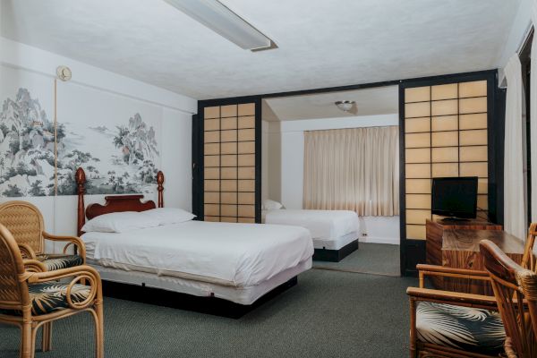 A spacious room with two beds, bamboo-style furniture, a TV on a wooden table, and a partition with shoji screens separating the two areas.